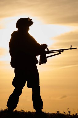Yaz akşamında üniformalı asker silueti ve makineli tüfek ya da saldırı tüfeği. Askeri ve savaş kavramı