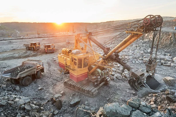 Mining industry. Heavy excavator loading granite rock or iron ore into the huge dump truck at opencast quarry. Sunset