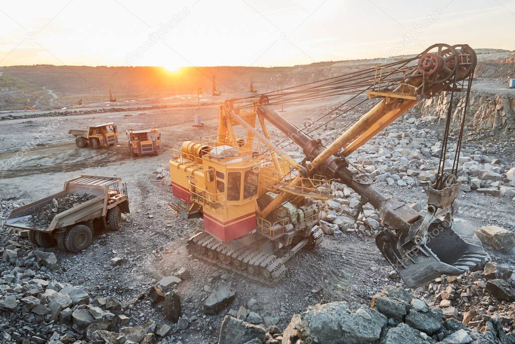 Mining industry. Heavy excavator loading granite rock or iron ore into the huge dump truck at opencast quarry. Sunset