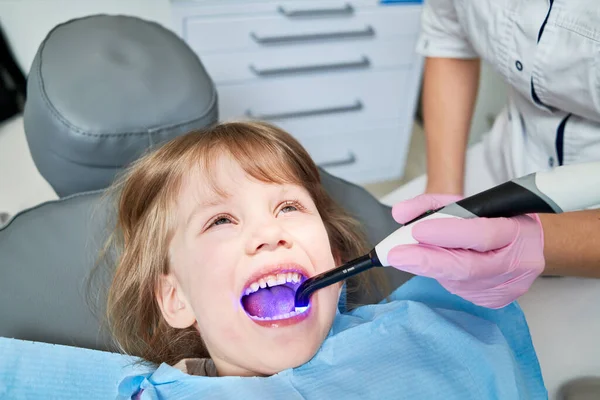 子供の歯医者 小さな女の子歯科検査 専門的な予防歯の洗浄と治療 医師は紫外線ランプを手に — ストック写真