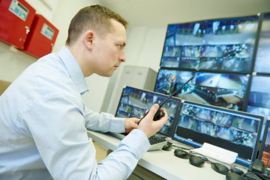 Güvenlik kamerası. Güvenlik görevlisi video izleme sistemini izliyor ve radyo vericisi kullanıyor.