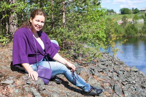 Mujer adulta sentada en rocas cerca de la orilla del río — Foto de Stock