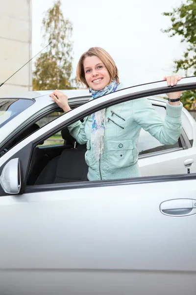 Joven mujer bonita de pie detrás de un coche con puerta abierta — Foto de Stock