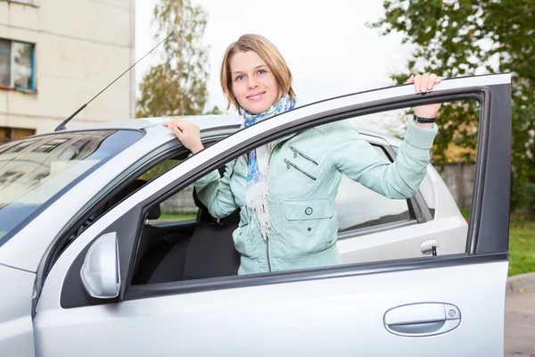 Young pretty Caucasain woman standing behind a car with opened door — Stock Photo, Image