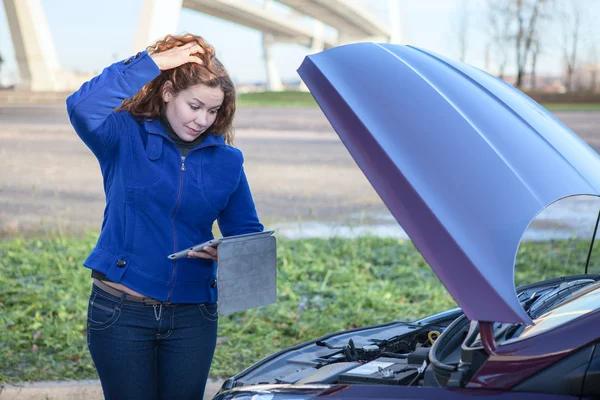 Gebroken voertuig met denken vrouw met tablet pc in de buurt van geopende motorkap — Stockfoto