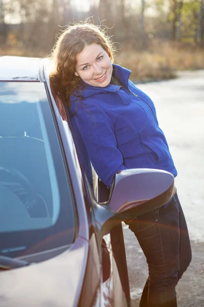 Gelukkig krullend haar vrouw leunde tegen auto in zon verlichting — Stockfoto