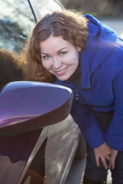 車の背面側のミラーの近くに立って、日光に対してカメラを見てきれいな女性 — ストック写真