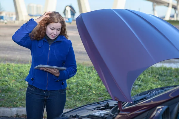 Thinking woman with opened car hood and tablet pc — Stock Photo, Image