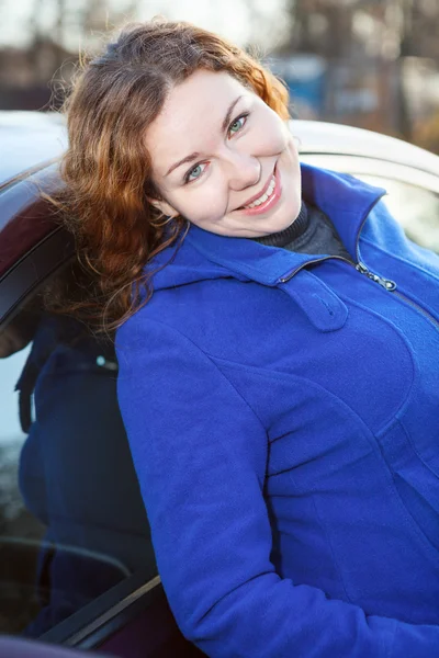 Mulher atraente inclinado para o carro sorrindo e olhando para a câmera — Fotografia de Stock