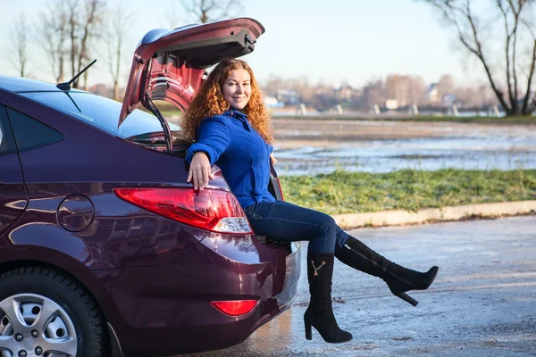 Attractive girl sitting in the car trunk — Stock Photo, Image