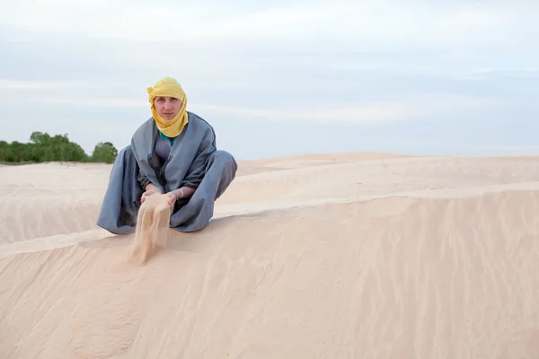 Caucasian person in protection eastern clothes pouring sand by hands on desert dune — Stock Photo, Image