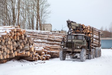 Log loader track with timber in lumber mill in winter season clipart