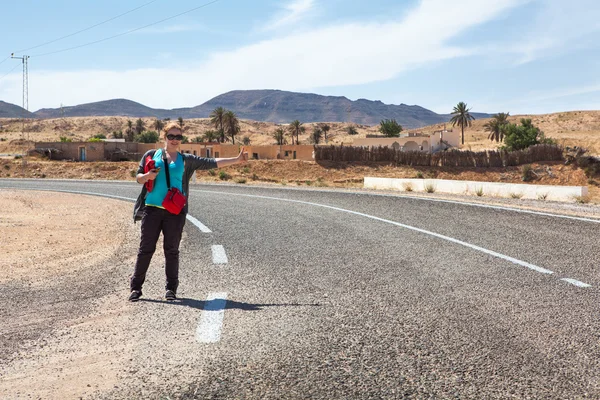 Woman on road with thumb lift up for hitching car — Stock Photo, Image