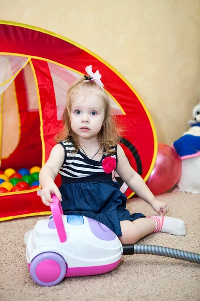 Criança pequena feliz brincando com aspirador de pó no quarto doméstico — Fotografia de Stock