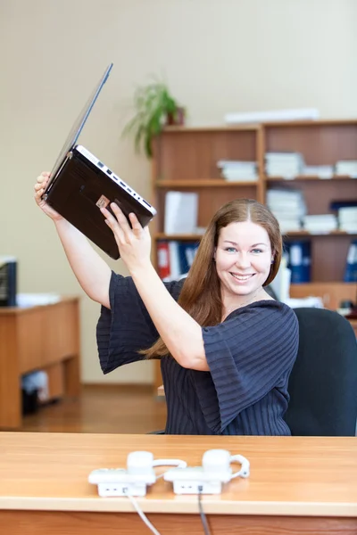 Giovane donna allegra che tiene il computer portatile sopra la testa mentre buone notizie in ufficio — Foto Stock