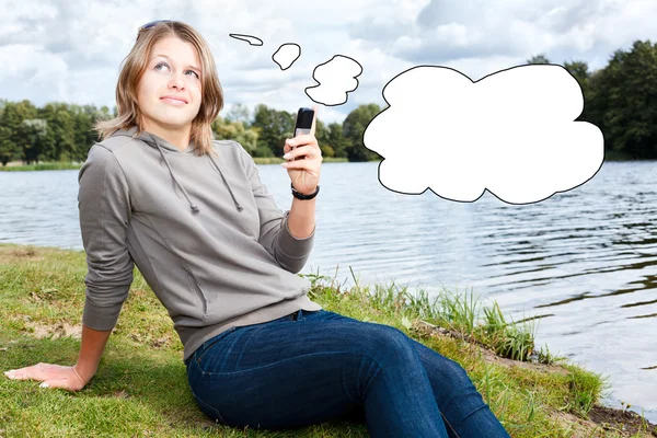 Mujer joven pensante con teléfono móvil y nube de pensamiento en blanco — Foto de Stock