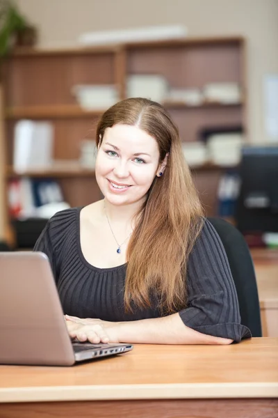Ευτυχής χαμογελαστό γυναίκα μελαχρινή με φορητό υπολογιστή στο γραφείο — Φωτογραφία Αρχείου