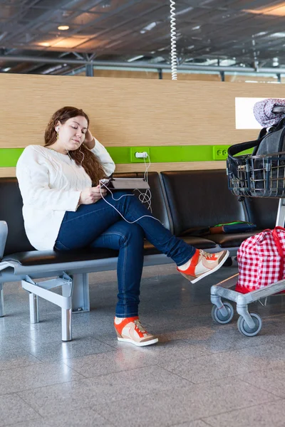 Mulher cansada, a olhar para o tablet pc no saguão do aeroporto com mão de bagagem-carrinho — Fotografia de Stock