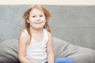 kurnaz bir sırıtma ile kanepede oturan dağınık saçlı küçük beyaz kız