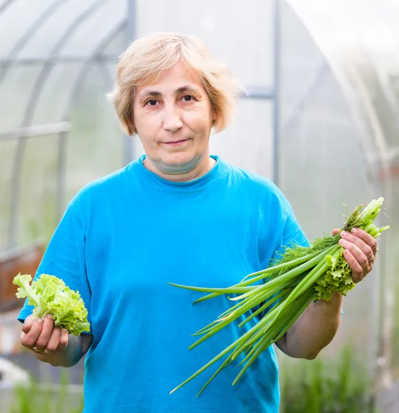 Happy mature woman with onion and lettuce in front of the greenhouse — Stock Photo, Image
