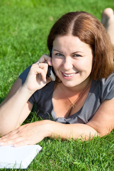 Giovane donna con libro che parla per telefono — Foto Stock