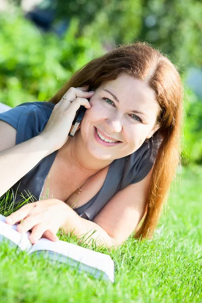 Ung kvinna med bok tala via telefon — Stockfoto
