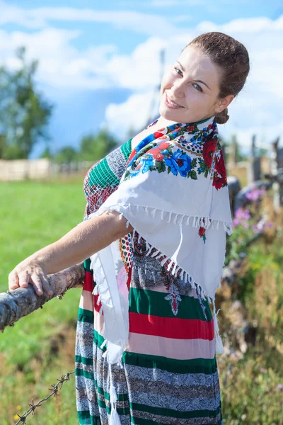 Красивая женщина, стоящая за забором в сарафане и платке — стоковое фото