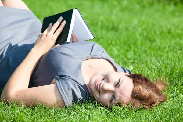 Vrouw terug opleggen groen gras met boek — Stockfoto