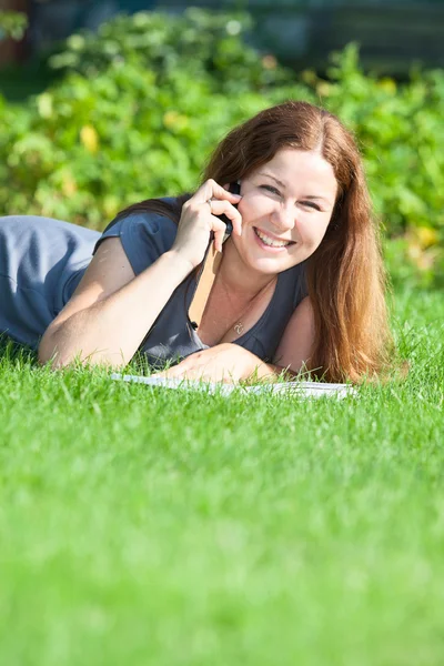 Ung kvinna med bok tala via telefon — Stockfoto