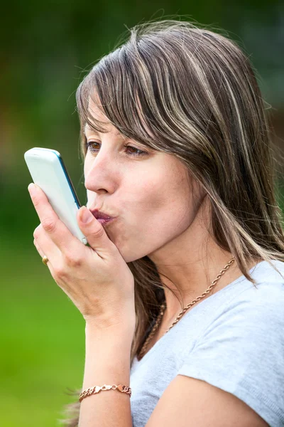Белая молодая женщина целует сотовый телефон на открытом воздухе — стоковое фото