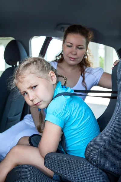 Unhappy girl sitting in child safety seat due mother fastening against the wishes — Stock Photo, Image