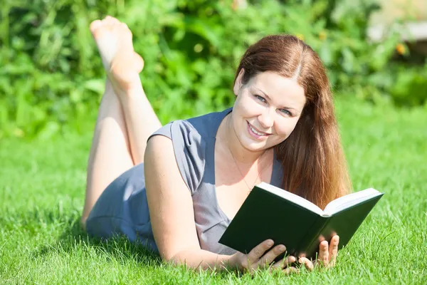 Woman lying on lawn with book Stock Photo