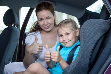 Mother and child showing thumb up gesture in car safety seat