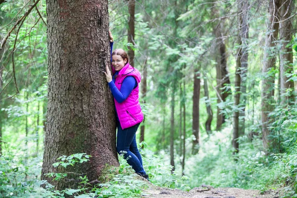 Tranquil mujer joven caucásica de pie mejilla a tallo de árbol en el bosque —  Fotos de Stock