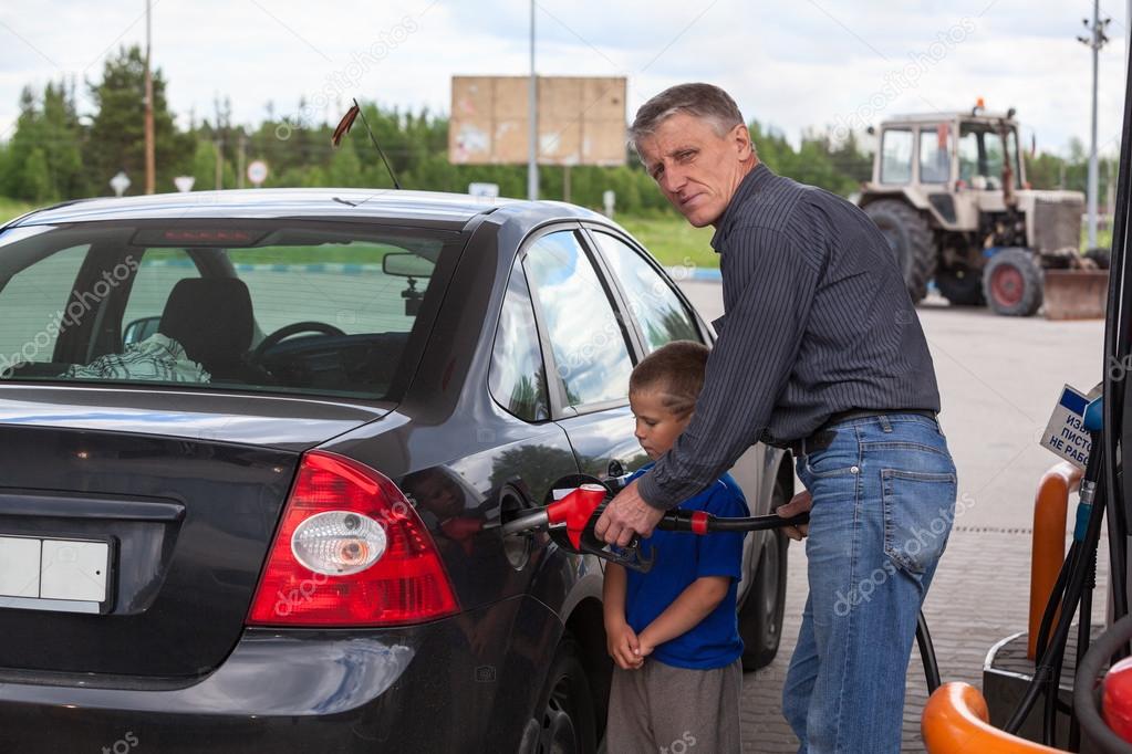 Young son looking at father refilling car at gas station