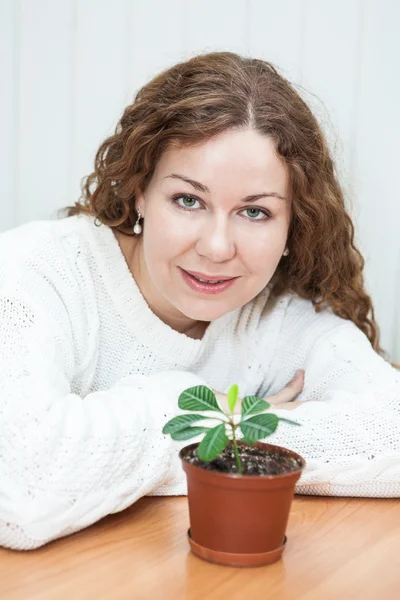 Jonge vrouw met groene plant zitten glimlachen — Stockfoto