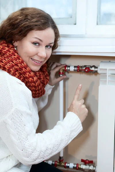 Mujer sonriente haciendo gestos al girar el termostato en la calefacción central —  Fotos de Stock