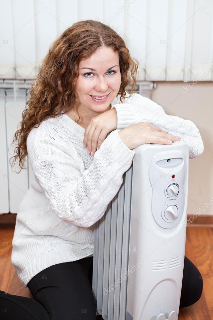 Portrait of long-haired curly woman near oil heater