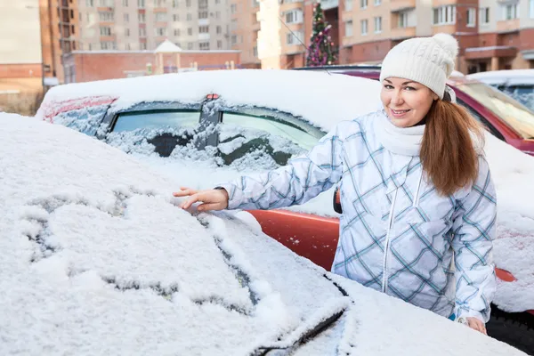 Frau zeichnet Herzform auf schneebedecktem Auto — Stockfoto