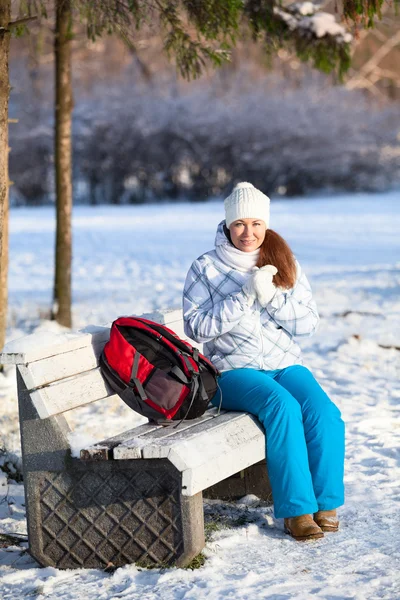 Mulher com mochila descansando em um banco no parque de inverno — Fotografia de Stock