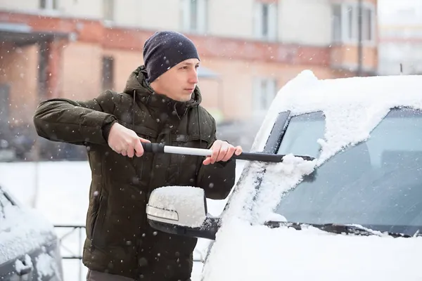 人从汽车前部除雪 从挡风玻璃上擦去积雪 — 图库照片
