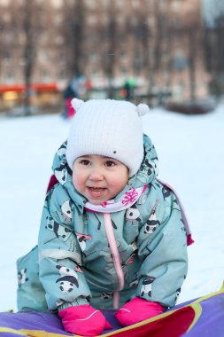 Kış mevsiminde şişme kızakla küçük beyaz bir kızın portresi, mutlu ve gülümsüyor.
