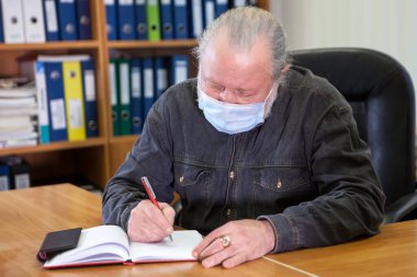Ofis odasında Covid-19 gribi nedeniyle kalemle maske takan kıdemli bir işadamı.