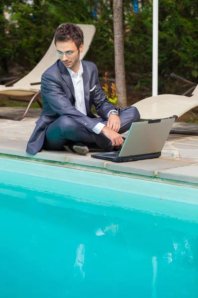 Jovem empresário com computador ao lado da piscina — Fotografia de Stock