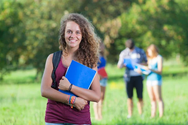 Jonge vrouwelijke student in het park met andere vrienden — Stockfoto