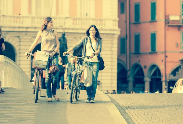 Dos hermosas mujeres caminando por la ciudad con bicicletas y bolsas —  Fotos de Stock
