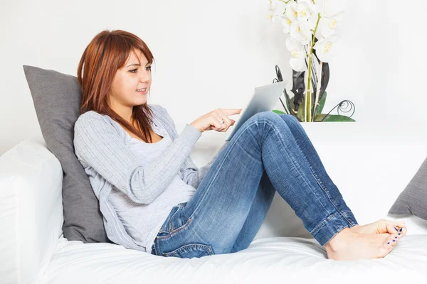Schöne junge Frau mit Tablet-PC auf dem Sofa — Stockfoto