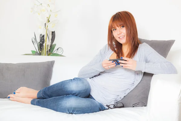Krásná mladá žena s smartphone na pohovce — Stock fotografie