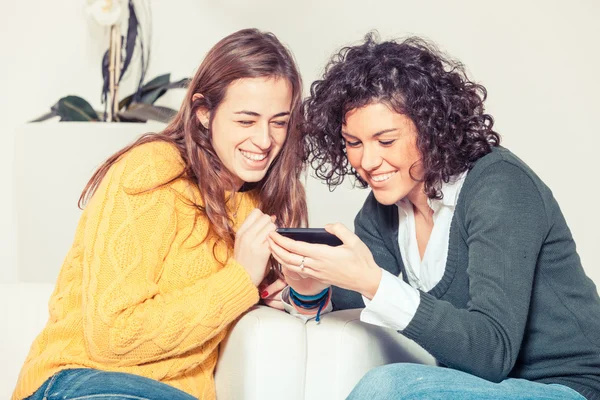 Twee mooie vrouwen met mobiele telefoon in de woonkamer — Stockfoto