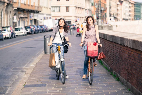 Zwei schöne Frauen, die mit Fahrrädern und Taschen durch die Stadt laufen — Stockfoto